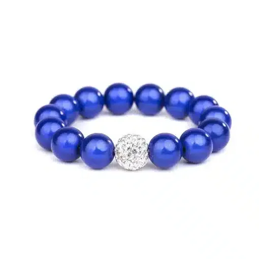 Das Magic Beads Ina Armband ist aus glänzenden blauen Perlen gefertigt und verfügt über eine einzelne runde, silberfarbene Perle, die mit kleinen, funkelnden Steinen verziert ist. Das Armband ist auf einem schlichten weißen Hintergrund abgebildet.