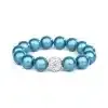 Das Magic Beads Ina Armband besteht aus einer Reihe glänzender blaugrüner Perlen, die um eine klare, funkelnde Perle zentriert sind. Dieses blaugrüne Perlenarmband ist kreisförmig vor einem schlichten weißen Hintergrund angeordnet.