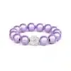 Das Magic Beads Ina Armband ist ein lila Perlenarmband mit einer einzelnen größeren Perle, die mit kleinen weißen Kristallen besetzt ist. Dieses exquisite Stück, das den Charme von Magic Beads hervorhebt, wird vor einem schlichten weißen Hintergrund präsentiert.