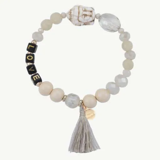 Das Buddha Love Armband ist ein Perlenarmband mit verschiedenen Perlen, darunter eine weiße Totenkopfperle, eine durchsichtige Perle und schwarze Perlen, die L,O,V,E ergeben. Es verfügt außerdem über ein kleines goldenes Etikett und ist mit einem grauen Quastenanhänger verziert.