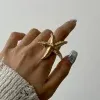 Entdecke deinen Look! Stell dir vor: Deine Hand, die einen beeindruckenden Beach Star Goldring trägt, stolz am Mittelfinger. Der edle Ring entfaltet seine ganze Wirkung über dem eleganten Beige deines Strickpullovers. Dazu glänzen deine Nägel in einem umwerfenden Metallic-Silber – der perfekte Kontrast zur schlichten weißen Wand im Hintergrund. Ganz klar, du setzt ein Statement!.