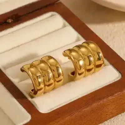 Die goldenen „Daily“-Ohrklemmen mit jeweils drei polierten Bändern werden in einer cremefarbenen Schmuckschatulle aus Holz präsentiert.