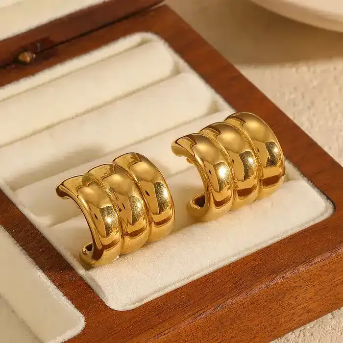 Die goldenen „Daily“-Ohrklemmen mit jeweils drei polierten Bändern werden in einer cremefarbenen Schmuckschatulle aus Holz präsentiert.