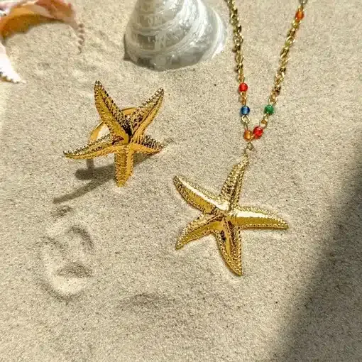 Entdecke The Beach Star und verleihe deinem Look das gewisse Etwas! Stell dir vor: ein zauberhafter Gold-Seestern-Ring und eine Kette mit einem Seestern-Anhänger an einer trendigen, bunt-perligen Kette. Das alles präsentiert auf sandigem Grund, umgeben von Muscheln – direkt aus den Tiefen des Meeres zu dir. Hol dir diesen Strandzauber und fühl dich wie die Königin der Wellen! 🌊✨.