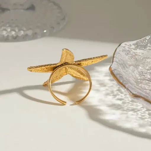 Entdecke The Beach Star – dein neues Must-have-Schmuckstück! Ein edler Goldring in Form eines Seesterns, der auf jede Hautfarbe strahlt und mit seiner zarten Silhouette pure Eleganz verkörpert. Stell dir vor, wie er auf einem hellen Untergrund funkelt und seinen faszinierenden Schatten wirft. Kombiniere ihn mit stylischen Glastellern und ihrer ausgefallenen Textur – ein echtes Highlight für jedes Fashion-Statement. Hol dir diesen einzigartigen Look und setze ein Zeichen am Strand oder in der Stadt!.