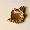 Entdecke die Meeresschönheit-Brosche, die dein Outfit auf ein neues Level hebt! Diese trendige Brosche in Gold-Optik ist wie eine Muschel geformt und besticht durch ihre strukturierten Details und blattartigen Elemente. Sie liegt sanft auf einem hellen Hintergrund und verleiht Ihrem Look einen Hauch von Eleganz. Lassen Sie sich von diesem modernen Accessoire inspirieren und setzen Sie ein stilvolles Statement!.