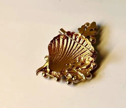 Entdecke die Meeresschönheit-Brosche, die dein Outfit auf ein neues Level hebt! Diese trendige Brosche in Gold-Optik ist wie eine Muschel geformt und besticht durch ihre strukturierten Details und blattartigen Elemente. Sie liegt sanft auf einem hellen Hintergrund und verleiht Ihrem Look einen Hauch von Eleganz. Lassen Sie sich von diesem modernen Accessoire inspirieren und setzen Sie ein stilvolles Statement!.