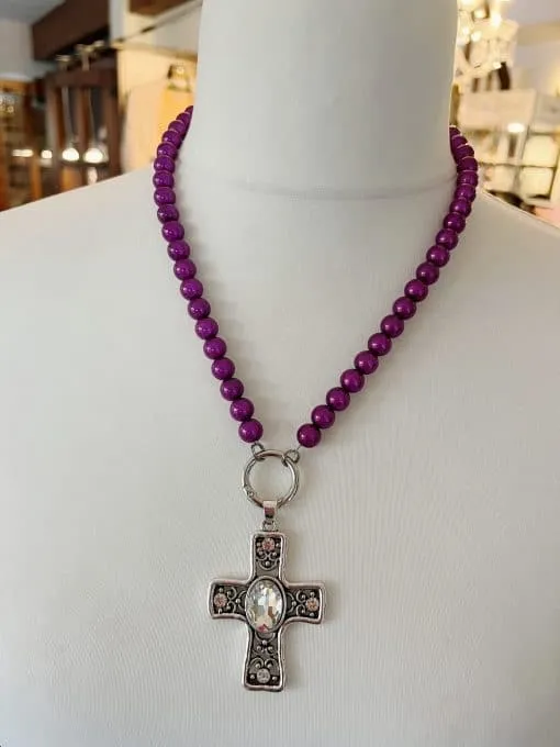 Entdecke die Magie! 🌟 Die Simple Halskette mit runden, violetten Perlen und einem silbernen Kreuzanhänger mit ovalem Schmuckstein wartet auf dich! Elegant inszeniert auf einer Büste, zieht dieses Schmuckstück alle Blicke auf sich. Die Umgebung aus stilvollen Regalen und sanften Lichtern verstärkt das magische Ambiente – genau das Richtige für Ihren individuellen Look. Gönn dir das gewisse Etwas und spüre die Faszination jeden Tag aufs Neue. ✨ Verleihe deinem Stil den ultimativen Touch von Glamour!.