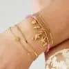 Schmücke dein Handgelenk mit purem Stil und einem Hauch von Meer! Stell dir coole goldene Delfintraum-Armbänder vor: Drei schlichte Bänder in kreisrunden und rechteckigen Formen, dazu eines mit lila Perlen und Meeres-Charms wie Seepferdchen, Muschel und Seestern – ein echter Hingucker! Zwischen all dem blitzt noch ein leichter Stoff hervor. Mach deinen Look einzigartig und zeige deine Liebe zum Ozean auf eine stylische Art und Weise. Mach's modern, mach's zu deinem Statement!.