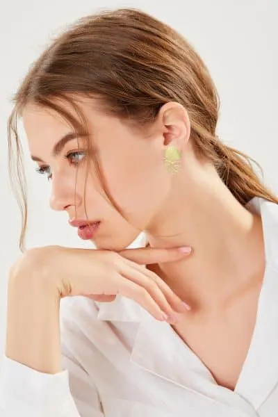 Stell dir vor, du bist die Frau mit dem im Nacken geschnürten braunen Haar und dem auffälligen goldenen Ohrring. Du ruhst deinen Kopf entspannt auf deiner Hand, während du seitlich in die Welt hinausblickst. In deinem eleganten weißen Shirt und vor einem sanft verschwommenen Hintergrund wirkst du wie das lebendige Symbol von Meer Liebe’s ästhetischem Zauber. Hier verschmelzen Stil und Ruhe zu einem perfekten Moment – genau wie bei dir!.