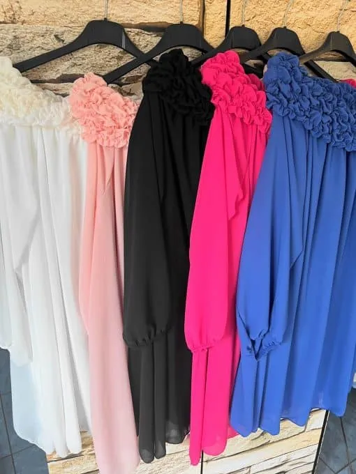 Stell dir vor, du trittst in dein Lieblingszimmer ein und entdeckst eine kleine Fashion-Oase: Fünf atemberaubende Sophia Chic Kleider reihen sich auf einer Stange an einer stilvollen beigen Steinwand auf. Von links nach rechts wartet ein Traum in Weiß, sanftem Rosa, klassischem Schwarz, strahlendem Pink und elegantem Blau darauf, von dir entdeckt zu werden. Jedes Kleid überrascht mit langen Ärmeln und einem verspielten Rüschenausschnitt – perfekt für dein nächstes Style-Statement! Lass deiner Kreativität freien Lauf und finde deinen Favoriten!.