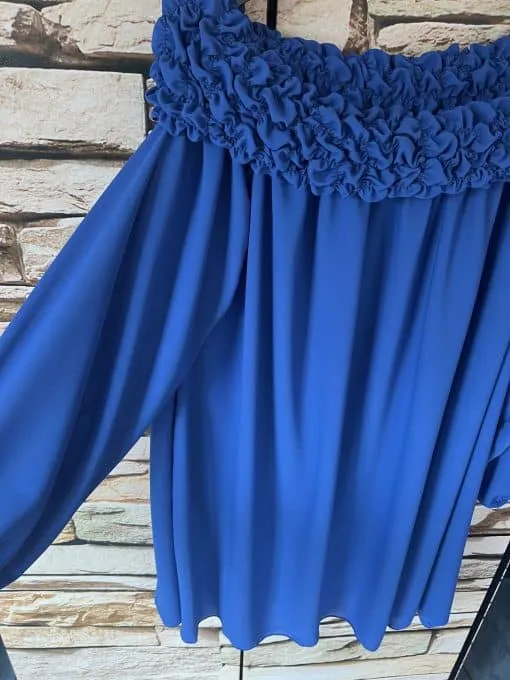 Entdecken Sie den unwiderstehlichen Charme der Sophia Chic! Diese trendige, schulterfreie Bluse in verführerischem Blau verleiht Ihnen dank ihres raffinierten Volant-Ausschnitts und lässig-langen Ärmeln einen eleganten Look. Perfekt inszeniert vor einer rustikalen Steinwand wird sie garantiert dein neues Lieblingsstück! Hol dir deinen Fashion-Moment jetzt und setze Statements mit Stil und Klasse.