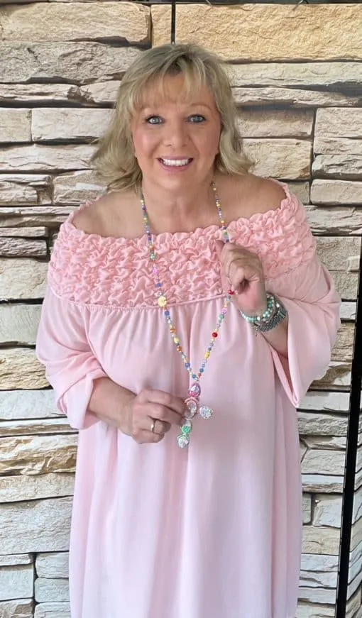 Stell dir vor: Du, mit deinem umwerfenden blonden Haar, in dem eleganten Sophia Chic Kleid in zartem Rosa. Dieses Off-Shoulder-Design schmeichelt deiner Figur und lässt dich strahlen! Dazu der Eyecatcher schlechthin: eine bunte Perlenkette mit einem beeindruckenden Anhänger, die du lässig in der Hand hältst. Und das alles für eine stylische Steinwand – ein Bild voller Fashion-Vibes und moderner Eleganz. Bereit, die Show zu stehlen?.