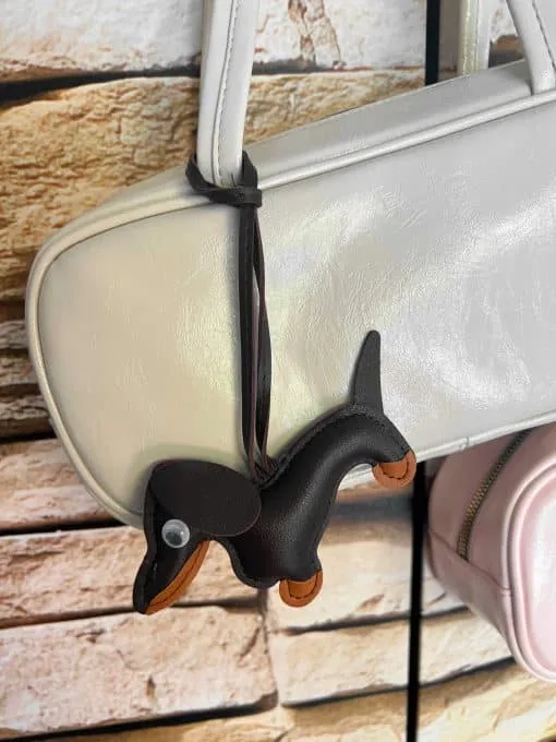 Entdecke deine neue Lieblingsbegleiterin: Die Dackel Love White Handbag! Dieses stylische Statement-Piece in strahlendem Weiß wird dich mit ihrem schwarzen Dackel-Anhänger verzaubern. Gegen den edlen Naturstein-Look im Hintergrund kommt das moderne Design besonders zur Geltung - bereit, jedes deiner Outfits aufzuwerten. Eleganz und Liebe zum Detail - trag deinen Style ab sofort immer bei dir!.