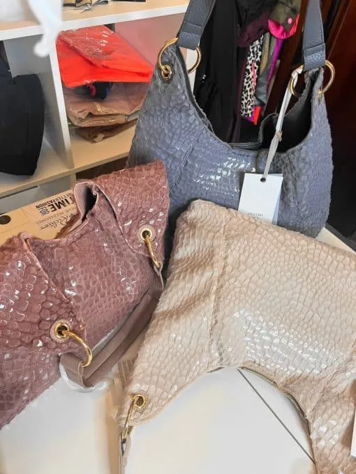 Entdecke deinen neuen Style: Drei trendige Handtaschen in Mauve, Grau und Creme setzen auf dem weißen Regal ein modernes Statement.