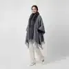 Trage den grauen Jolina Poncho Schal mit Fell und Fransen zu weißen Hosen und Heels - dein moderner Look für selbstbewusste Auftritte!.