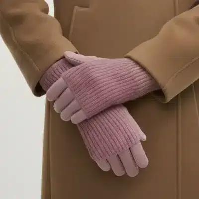 Du trägst einen braunen Mantel und setzt mit den gerippten pinken Rosalind Handschuhen ein stylisches Statement.