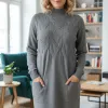 Du trägst das Cable Chic Dress in einem stylischen, gemütlichen Wohnzimmer mit Bücherregalen und üppigen Pflanzen.