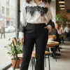 Erlebe den modernen Look: Du trägst die Bella Lace White Bluse, stylishe schwarze Hosen und Boots im angesagten Café am Fenster.