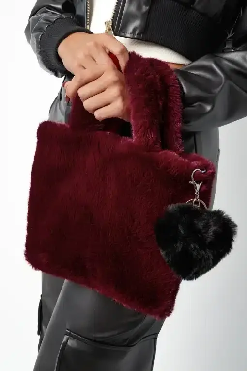Du hältst eine bordeauxrote Faux-Fur-Handtasche mit schwarzem Plüsch-Liebesanhänger zu deinem coolen Lederlook.