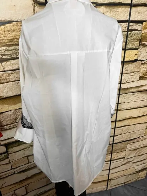 Entdecke deinen Style: Die Bella Lace White Bluse mit langen Ärmeln zeigt sich modern vor einer angesagten Steinwand.