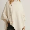 Du stehst im Mittelpunkt: Im cremefarbenen Dinah Poncho mit stylishen Seitenknöpfen und schwarzen Hosen bist du ein Hingucker.