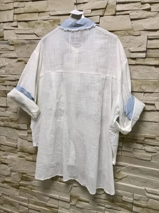 Entdecke deinen Style: Trag dieses lässige, weiße Shirt mit blauen Akzenten und aufgerollten Ärmeln - modern am Stein gehängt.