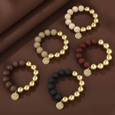 Entdecke deinen Style mit fünf modernen, perlenbesetzten Armbändern und goldenen Akzenten - trendy präsentiert auf braunem Hintergrund.