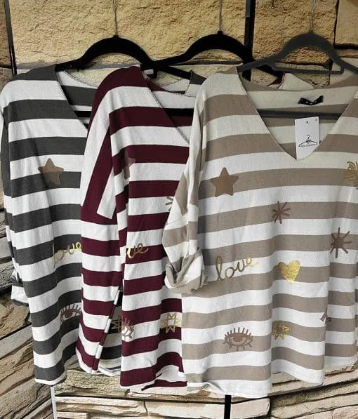 Erlebe trendige Streifen-Langarmshirts mit goldenen Prints - edel präsentiert an schwarzen Bügeln vor einer Steinwand.