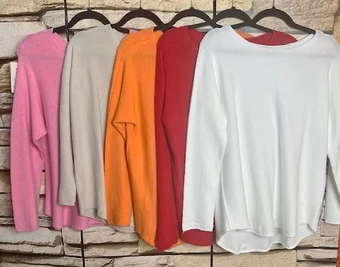 Erlebe den modernen Style: Fünf Soft Line Pullover in Trendfarben warten an eleganten Haken vor rustikalem Stein auf dich!.