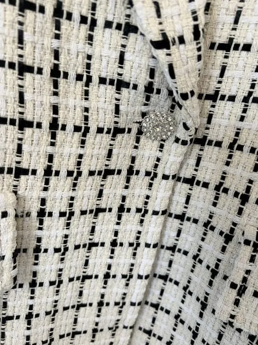 Spür die edle Struktur des schwarz-cremefarbenen Karostoffs und entdecke den funkelnden Knopf am Blazer 