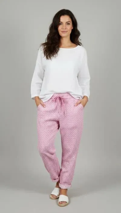 Erlebe den Zauber: Du strahlst in weißem Longsleeve und der zauberhaften Relax Hose mit pinken Mustern vor grauem Hintergrund.