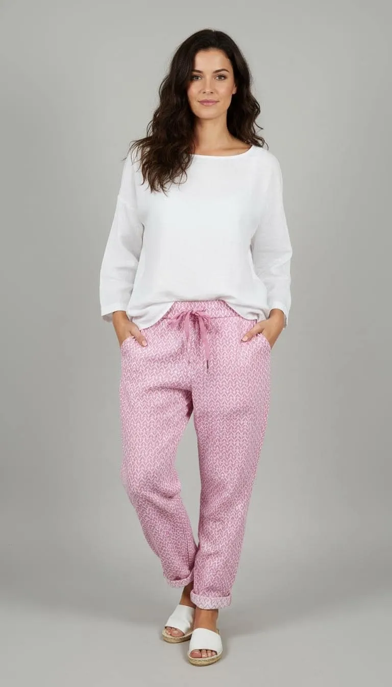 Erlebe den Zauber: Du strahlst in weißem Longsleeve und der zauberhaften Relax Hose mit pinken Mustern vor grauem Hintergrund.