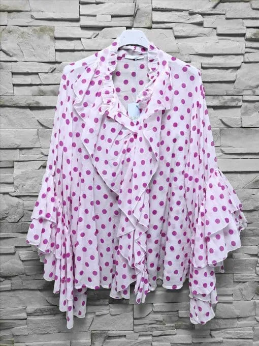 Hol dir den Punkteprinzessin-Look: Weiße Rüschenbluse mit pinken Punkten vor Steinwand - für deinen auffälligen Style!.