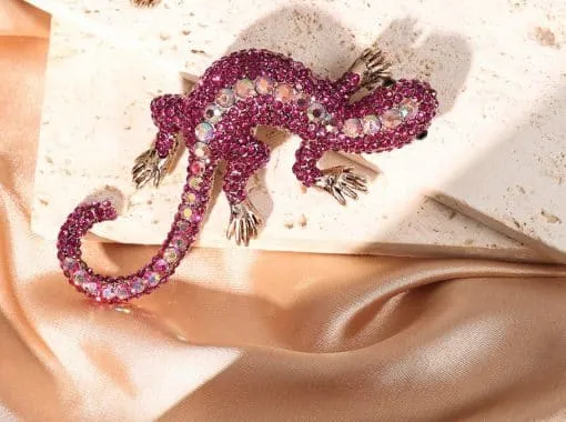 Erlebe die Geko Brosche - ein funkelnder Eyecatcher mit pinken, irisierenden Steinen auf edlem Stein und Satin für deinen Style.