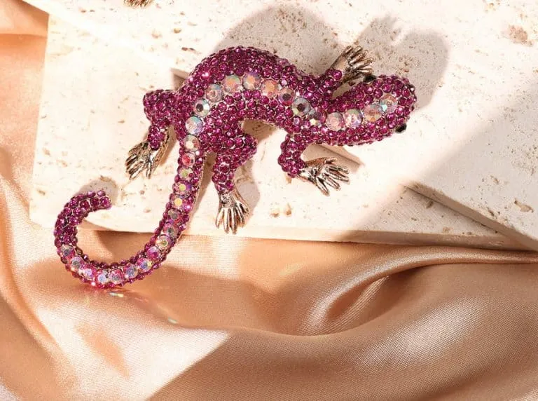 Erlebe die Geko Brosche - ein funkelnder Eyecatcher mit pinken, irisierenden Steinen auf edlem Stein und Satin für deinen Style.