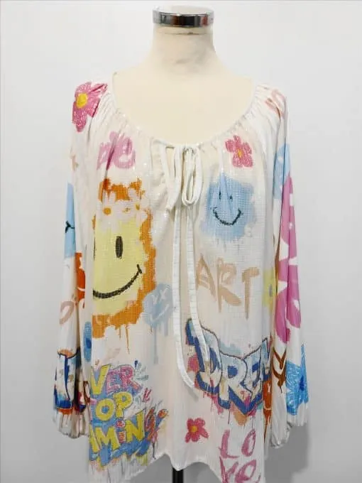 Zieh dir die Dream Love Tunikabluse an: Ein weißes Longsleeve mit bunten Smileys und inspirierenden Botschaften wie DREAM, LOVE & OVERCOMING.