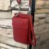 Entdecke deine neue Lieblings-Bag: Die kleine rote Ledertasche mit Handgelenkschlaufe setzt moderne Akzente vor urbaner Steinwand.