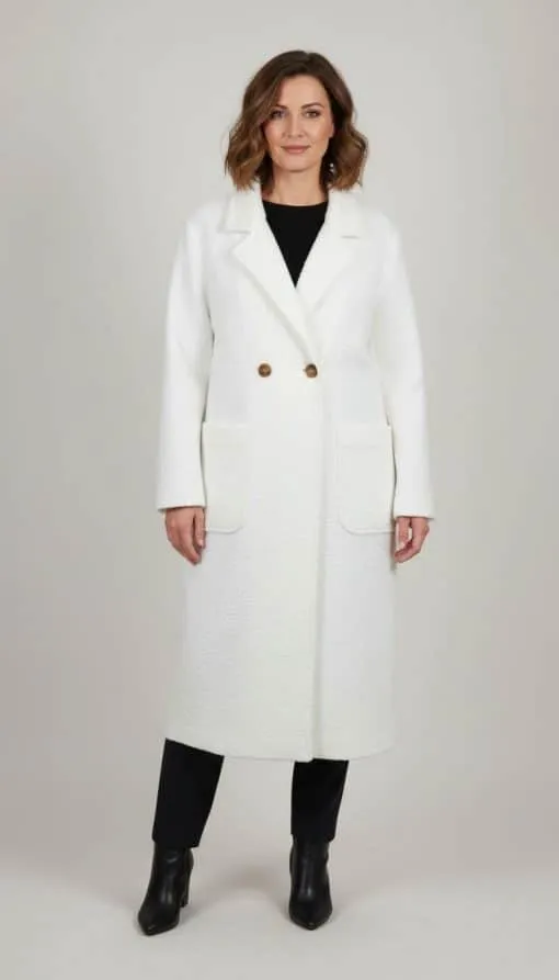 Du trägst den Cozy Long Mantel in Weiß, doppelt geknöpft und mit großen Taschen - kombiniert zu schwarzen Hosen und Ankle Boots.