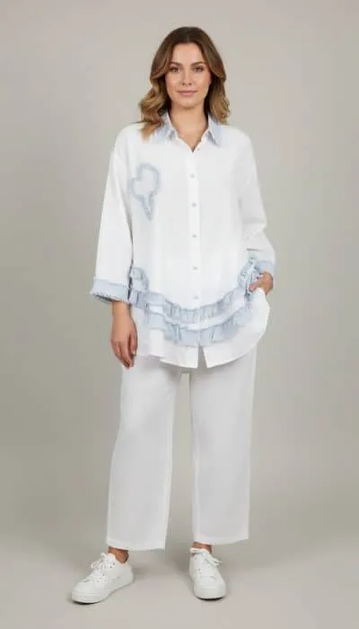 Du setzt ein modernes Statement: Lässiges weißes Outfit mit blauen Akzenten und Sneakern vor cleanem, hellem Hintergrund.