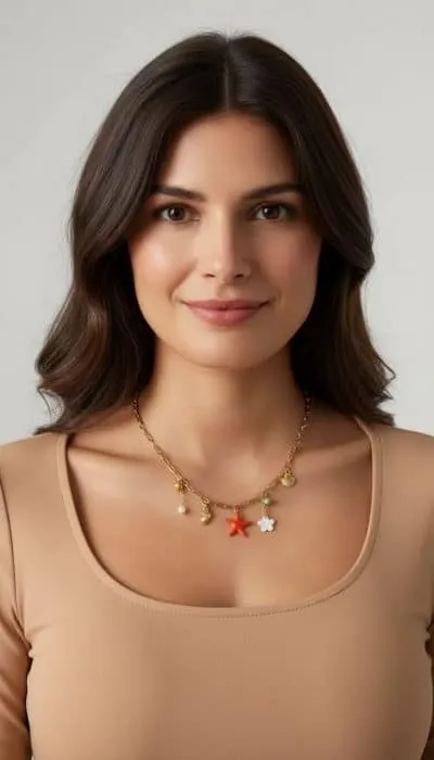 Du strahlst stilvoll mit welligem, braunem Haar, beigem Top und der goldenen Sand & Meer Sommer-Charm-Kette in bunten Farben.