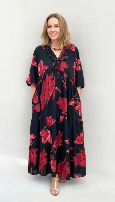 Home Du trägst ein lässiges schwarzes Kleid mit auffälligem roten Blumenprint und strahlst entspannt vor einer hellen Wand.