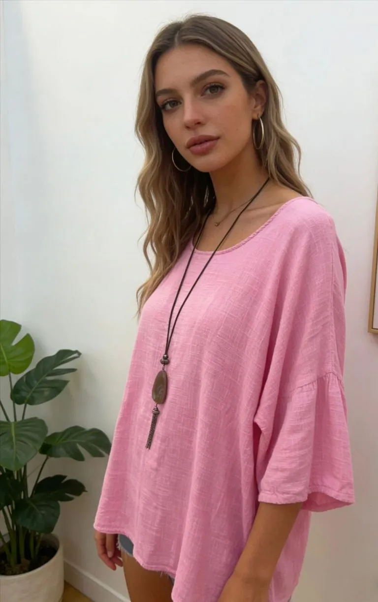 Frau modelliert locker sitzendes rosa Leinenlook-Tunika-Shirt, das mit seinem atmungsaktiven Leinenstil für Komfort und Vielseitigkeit im Haus sorgt.