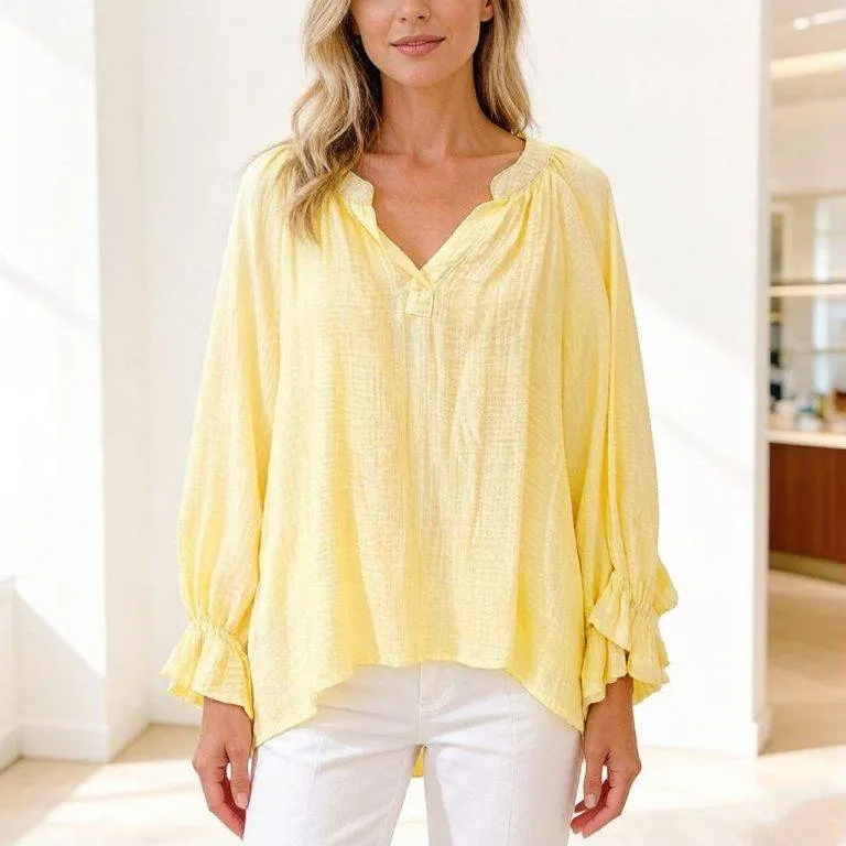 Eine Frau trägt die Sunny Breeze Tunikabluse - lockere Passform, lange Ärmel, geraffter Ausschnitt, gerüschte Manschetten - für luftigen Komfort und Stil.