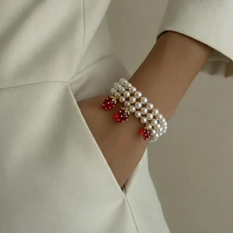 Beeren-Perlenarmband: Dreireihiges Armband mit Erdbeeranhängern am Handgelenk einer Frau.