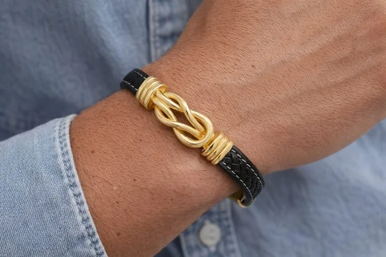 Knoten Unisex Armband: Nahaufnahme eines schwarzen Lederarmbands mit goldenem Knoten auf einem Handgelenk.