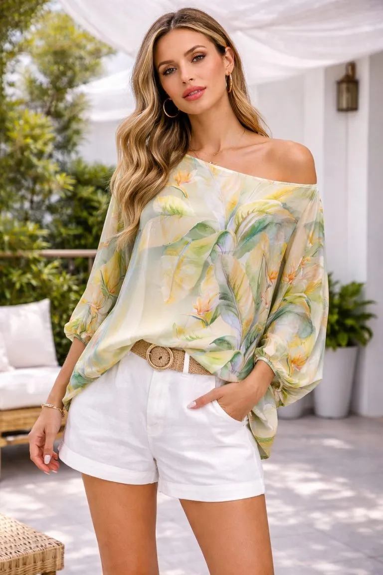 Frau in tropischer Bluse und weißen Shorts. Sommerliches Modeoutfit mit Pflanzenmuster und Strohgürtel.