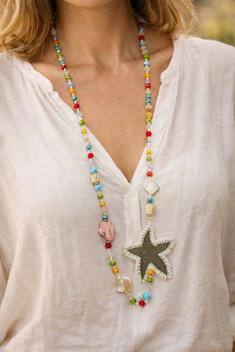 Das Model präsentiert die Happy Garden Kette, eine Statement-Halskette mit Stern-Anhänger und bunten Perlen, die jedes Outfit aufwertet.