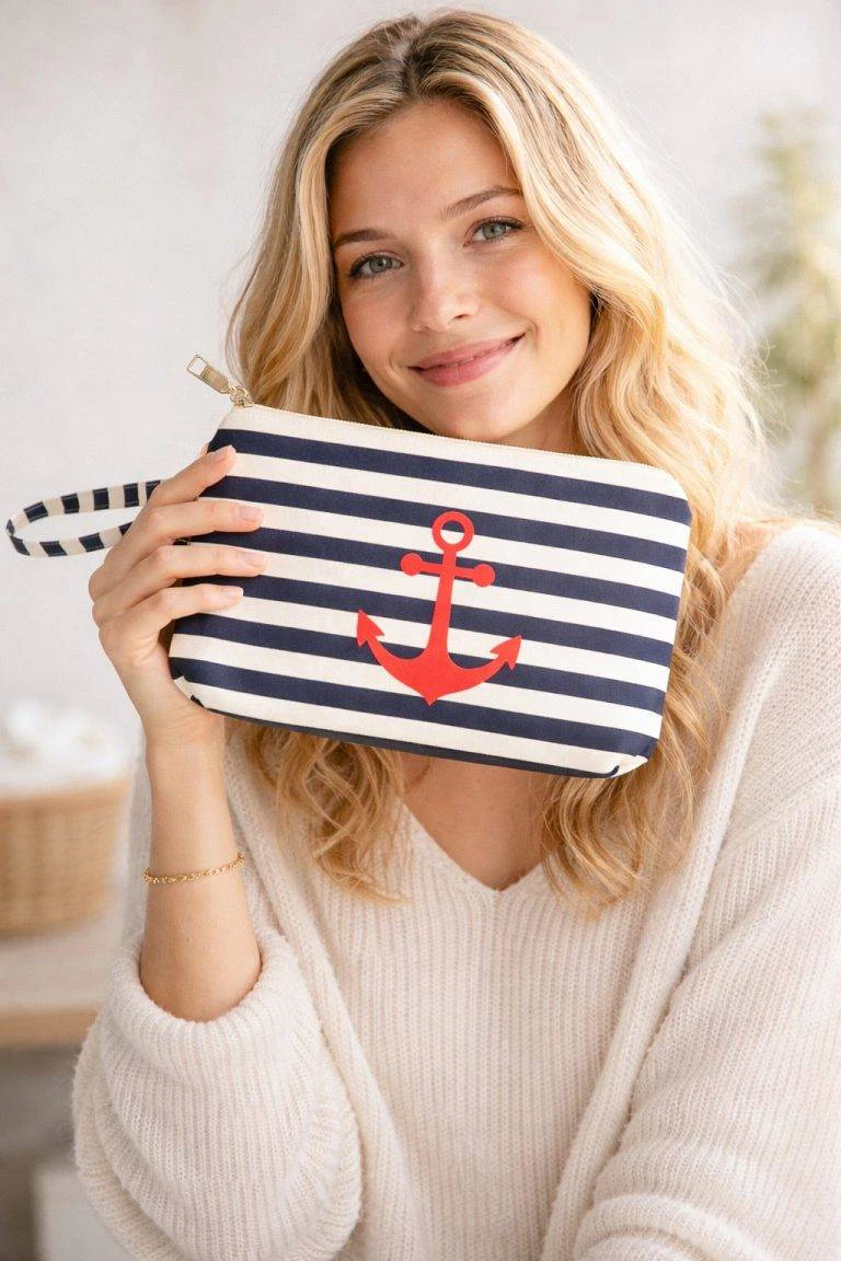 Eine lächelnde Frau hält die Ahoi Beauty Tasche - ein stilvolles marineblaues und weißes Etui mit rotem Anker, ideal für Reisen, Make-up und Organisation.