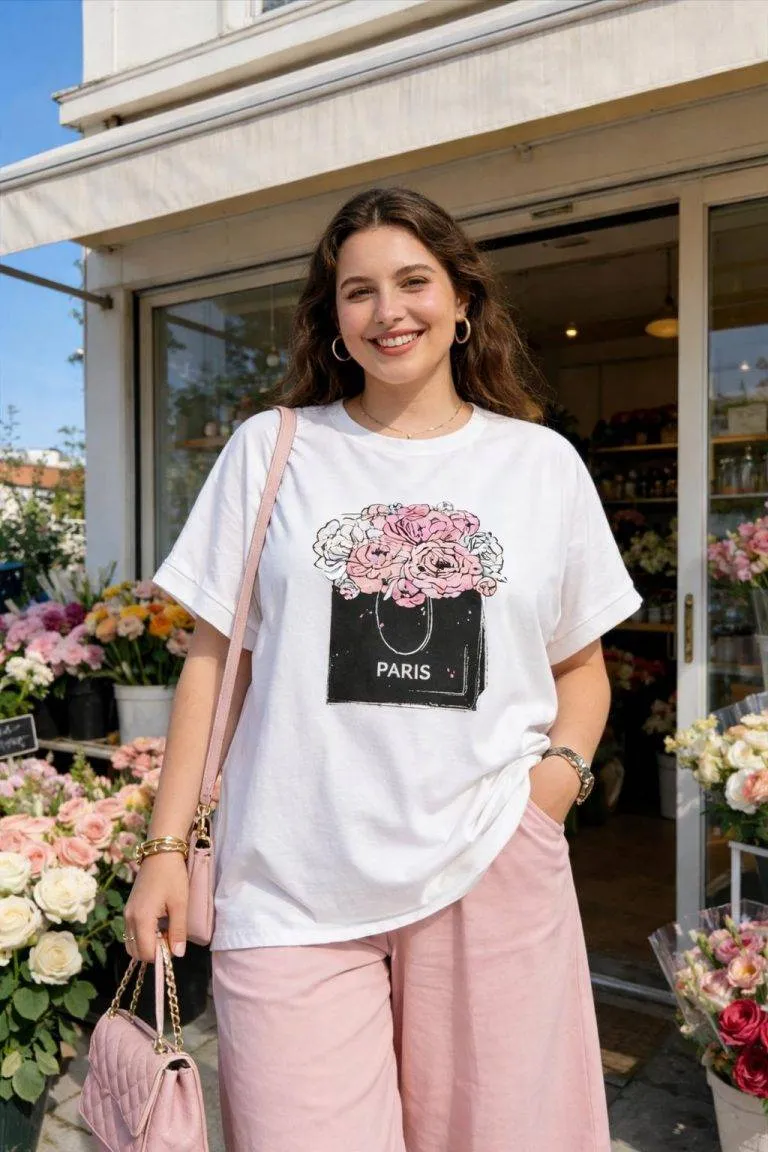 Rosé Romance Shirt Modell mit Paris-Motiv. Frau mit Blumen-T-Shirt und rosa Hose vor Blumengeschäft.